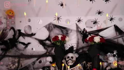 Media: A video depicts a Halloween-themed altar with black and white skulls, a white skeleton, red and white flowers, and hanging bats. The background is adorned with spider decorations and lit candles, creating a spooky, festive atmosphere.