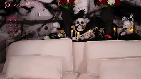 Media: A video of a Halloween-themed living room featuring a white couch, a skull on a black pillow, a black skeleton, and red and white flowers, set against a dark, abstract wall.