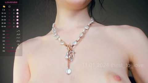 Media: Video of a topless, light-skinned Asian woman with black hair, wearing a pearl necklace with a pendant. Background is blurred, and a calendar app is visible in the top left corner.