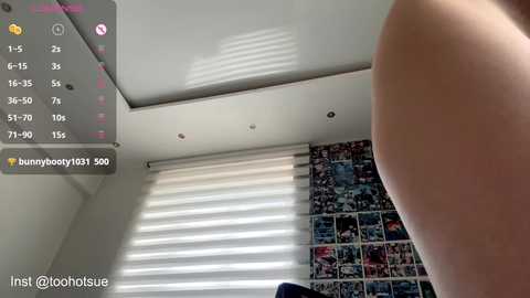 Media: Video of a person's bare buttocks, captured from a low angle, in a brightly lit room with white blinds partially drawn, showcasing a colorful wall of photos.