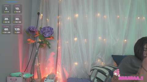 Media: A video of a cozy room with white sheer curtains, purple and orange flowers, a teal and white striped pillow, and a person in a gray shirt, partially visible.