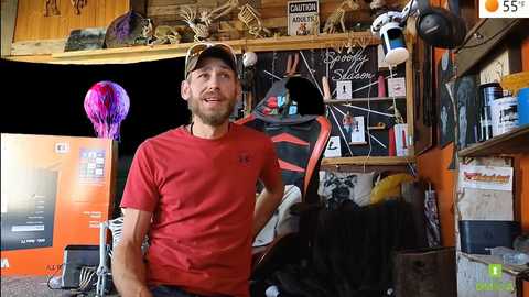 Media: Video of a bearded man in a red t-shirt and baseball cap standing in a cluttered, brightly-lit workshop. Background includes various tools, a helmet, and a vibrant balloon.