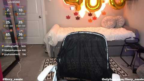 Media: A video of a cozy bedroom with a gray bed, white bedding, and golden \"2020\" balloons. A black backpack and white shoes are foreground objects.