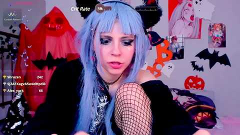 Media: Video of a young woman with light blue hair, wearing a black outfit, fishnet stockings, and cat ears, in a Halloween-themed room with decorations and emojis.