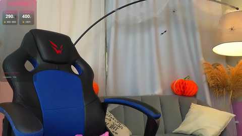 Media: Video of a modern gaming chair with blue and black upholstery, orange pumpkins, and a white wall with a lamp and decorative items.