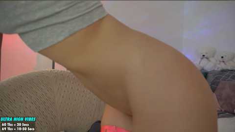 Media: Video of a person wearing a grey top, bending over to reveal their buttocks clad in sheer black tights. The background features a beige cushion and a blurred, cozy indoor setting.