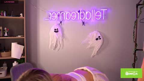 Media: Video of a cozy bedroom with two hanging white ghost decorations, \"Happy Halloween\" neon sign, and a bed with a person in a white shirt visible.