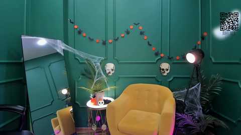 Media: Video of a vibrant, Halloween-themed room with teal walls, a yellow armchair, a small round table with a potted plant, a spider web, skulls, and orange lights.