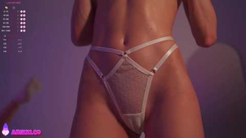 Media: Video of a nude woman with light skin wearing strappy, sheer, metallic silver thong lingerie, standing indoors against a purple backdrop.