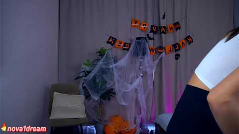 Media: A video captures a Halloween-themed room with a white bed, grey curtains, a green chair, a pumpkin, a spiderweb, and \"ween world\" banners.