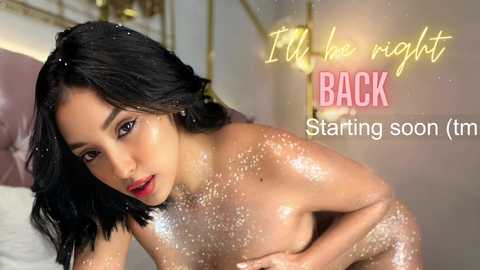 Media: Video of an Asian woman with long black hair, wearing glittery body paint, posing seductively in a bed. Text overlay reads, \"The night is back starting soon (tm).\