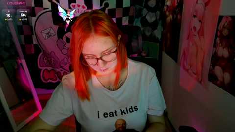 Media: Video of a young woman with straight, bright red hair, glasses, and a \"I eat kids\" t-shirt, seated in a dimly lit room with a checkered wall and anime posters.