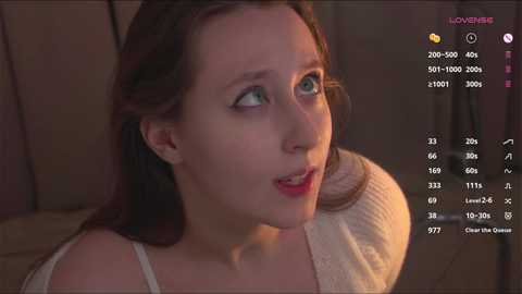 Media: Video of a young Caucasian woman with fair skin and brown hair, wearing a white tank top, looking surprised in dim lighting.