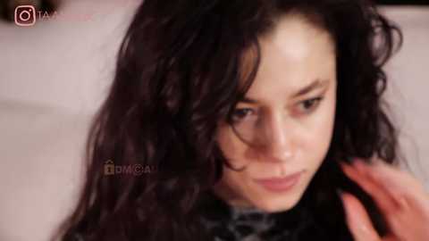 Media: A video of a young woman with long, wavy black hair and pale skin, looking introspective, with a blurred background. She wears a black top, and the image has a watermark that says \"DMG\".