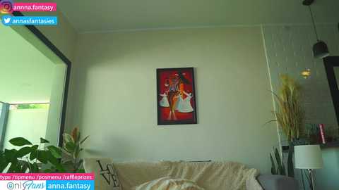 Media: A video of a modern living room featuring a large framed painting of three people dancing, beige couch with a plush throw, and a potted plant.