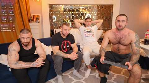 Media: Video of four shirtless, tattooed men sitting on a blue couch in a modern living room with hexagonal-patterned glass wall and golden curtains.