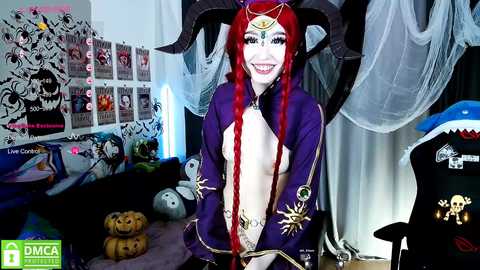 Media: Video of a cosplay enthusiast in a dark, gothic-themed room, dressed as a red-haired, horned demoness with elaborate makeup, surrounded by Halloween decorations and gaming equipment.