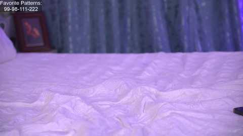 Media: A video of a bed covered in a white, wavy-patterned comforter. The background features a dark, patterned curtain. Text in the top left corner reads \"Favonie Patterns: 99-09-111-1222.\