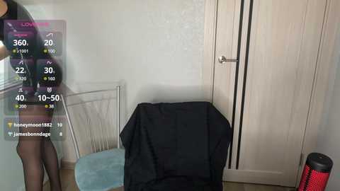 Media: Video of a woman in a black dress, standing in a bedroom with a white door, a blue chair, and a black coat draped over a chair.