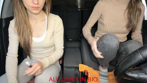 Media: A video of a young woman with long brown hair, wearing a beige sweater and grey pants, seated in a car, looking contemplative.