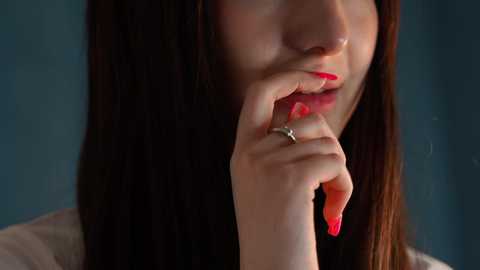 Media: Video of a young woman with long dark hair, pale skin, and red lipstick, holding a cigarette to her lips, wearing a silver ring on her left hand.