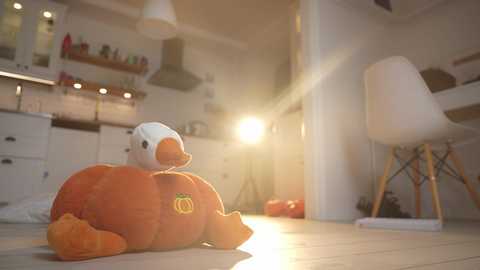 Media: Video of a plush duck in a pumpkin costume lying on a wooden floor in a modern kitchen with white cabinets, a large window, and white chairs.