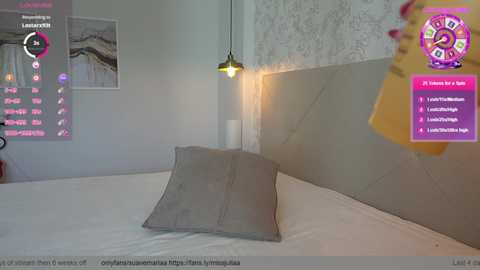 Media: Video of a minimalist bedroom with a beige headboard, white sheets, and a gray pillow. A pink clock and a neon light are visible.