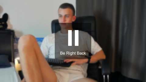 Media: Video of a young man in a grey T-shirt, white shorts, sitting on a black chair, legs crossed, typing on a laptop, with the words \"Be Right Back\" overlaid.