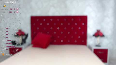 Media: A video of a modern bedroom featuring a red tufted headboard, white bed, red pillows, and two matching red nightstands with lamps. The background is a white, textured wall.