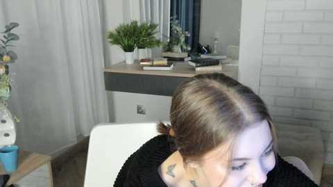 Media: A video of a salon chair with a woman's head partially visible, light brown hair in a bun, wearing a black top. Background shows a desk with plants, books, and a mirror.