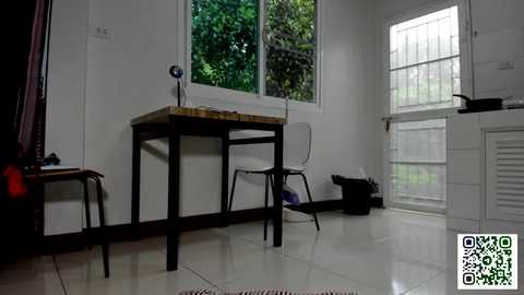 Media: Video of a minimalist, white-walled room with a wooden desk, metal chair, and large window overlooking greenery. A black trash bin and a QR code are visible.