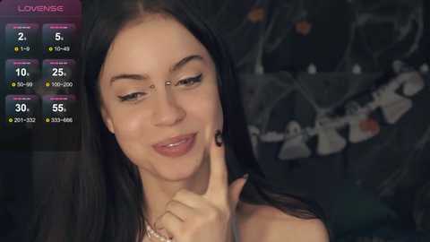 Media: Video of a smiling woman with long dark hair, wearing black lipstick, in a dimly lit room with a blurred background featuring a dark, possibly gothic, aesthetic.