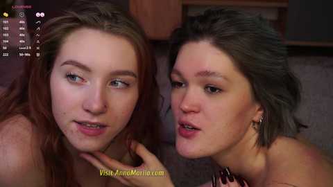 Media: Video of two young women with fair skin, one with long brown hair, the other with short black hair, both wearing makeup, in a close-up, intimate setting.