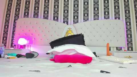 Media: Video of a playful bedroom scene with a stuffed pilot doll on a bed covered in a white sheet, surrounded by toys, a black and white striped wall, and a tufted headboard.