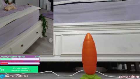 Media: Video of a realistic, large, orange carrot-shaped dildo on a white bed frame in a modern bedroom, with a pink and purple bedspread and a green pillow.