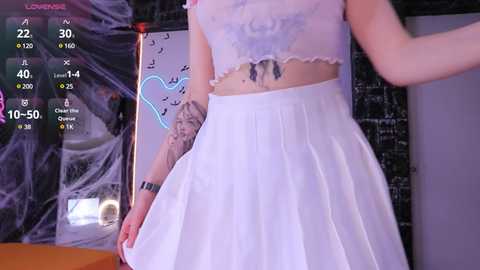 Media: A video of a young woman with light skin, wearing a white lace crop top and high-waisted pleated skirt, posing in a dimly lit room with a spider web backdrop and glowing neon heart.