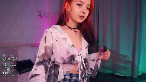 Media: Video of an Asian woman with long, dyed orange hair, wearing a white tie-dye crop top and plaid skirt, standing in a dimly lit room with a bed and purple lighting.