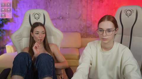 Media: Video of two young women in gaming chairs; one with glasses, another with long hair, in a modern, dimly lit room with purple and red lighting.