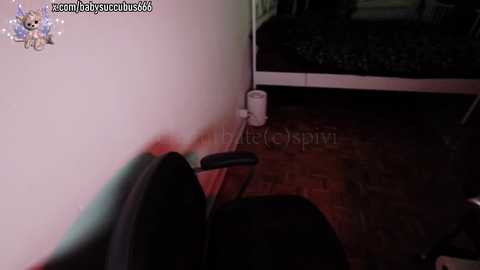 Media: A dimly lit video shows a corner of a room with a white wall, a black chair, a white trash can, and a partially visible bed with dark bedding.