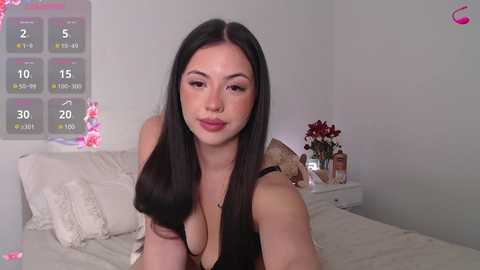 Media: A video of a young, fair-skinned woman with long black hair, wearing a black lace top, smiling in a minimalistic, white-walled bedroom.