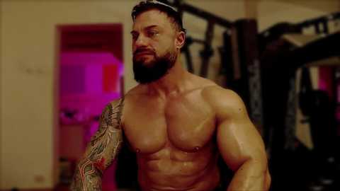 Media: Video of a muscular, shirtless man with a full beard and tattoos, working out in a gym with purple lighting, showcasing his defined chest and arms.