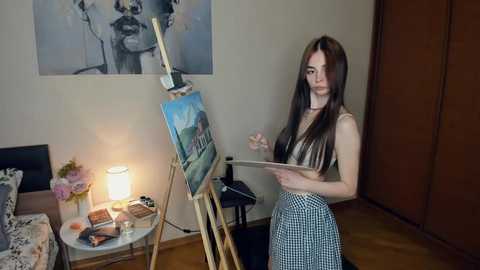 Media: A video of a young woman with long, straight brown hair, wearing a sleeveless top and checkered skirt, painting on an easel in a brightly lit, minimalist room with a large abstract painting on the wall.