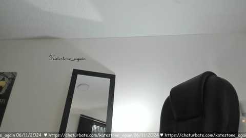 Media: Video of a minimalist room with white walls, a black-framed mirror, and a hanging black jacket. The ceiling is sloped, and the room appears clean and uncluttered.