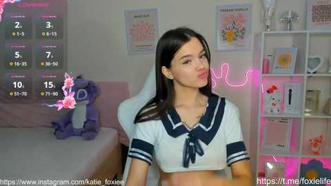 Media: Video of a young Asian woman with straight black hair, wearing a schoolgirl outfit, sitting on a white gaming chair in a room with pink neon lights, plush toys, and posters.