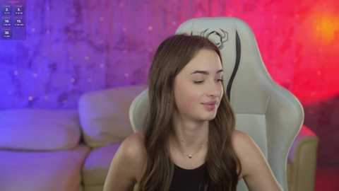 Media: Video of a young woman with long brown hair in a black tank top, sitting in a white gaming chair with a red and purple LED background.