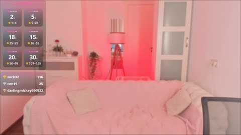 Media: A video of a modern, minimalist bedroom with a pink light. The room features a white sofa, a white door, and a small table with a plant.