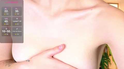 Media: A video of a topless person with fair skin, medium-sized breasts, and a hand lightly pressing on one breast. The background is blurred, featuring green foliage.