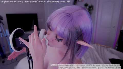 Media: Video of a pale-skinned woman with purple hair, elf ears, and glasses, using a white microphone, in a dimly lit room. Text overlays include URLs and a watermark.