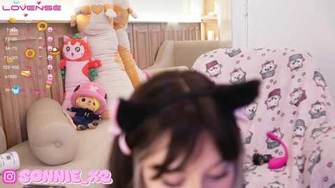 Media: A video shows a person in a pink cat costume, sitting on a couch with plushies, including a pink bear and a cat.