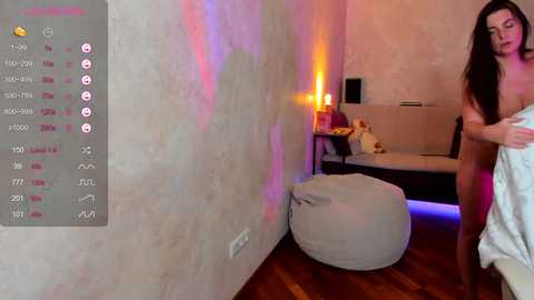 Media: A video captures a nude woman with long hair, standing in a dimly lit room with a white pouf, a candle, and a calendar.